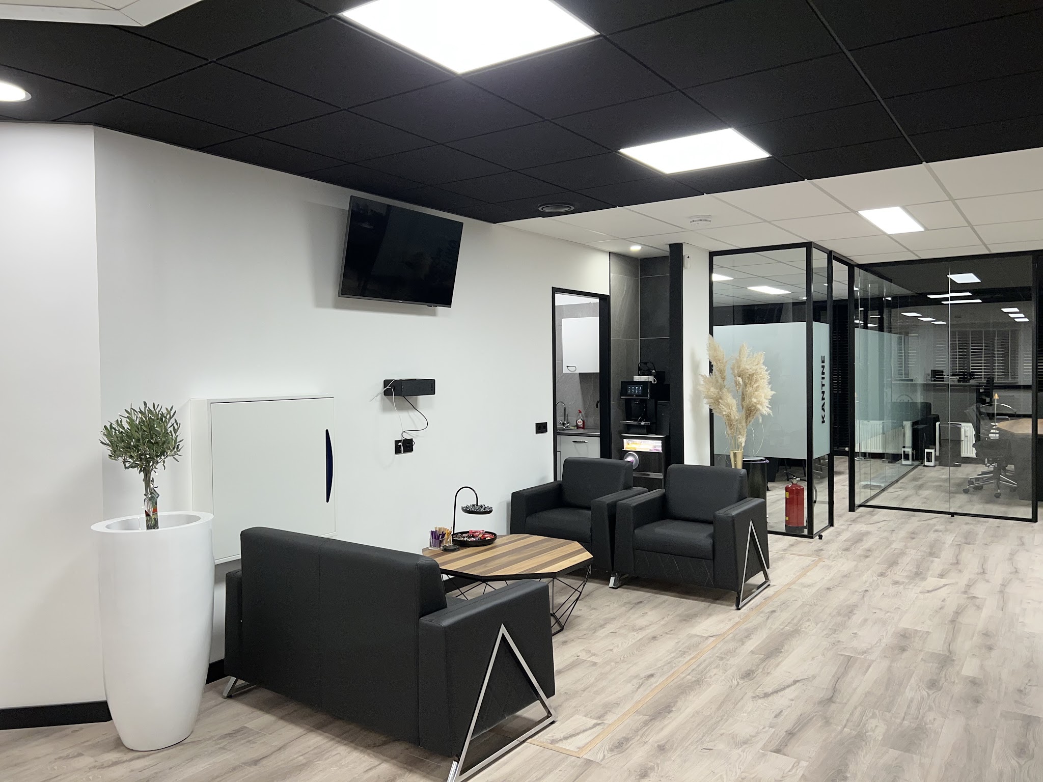 Kantoorlounge met zwarte fauteuils, LED-panelen in een zwart systeemplafond en glazen wanden
