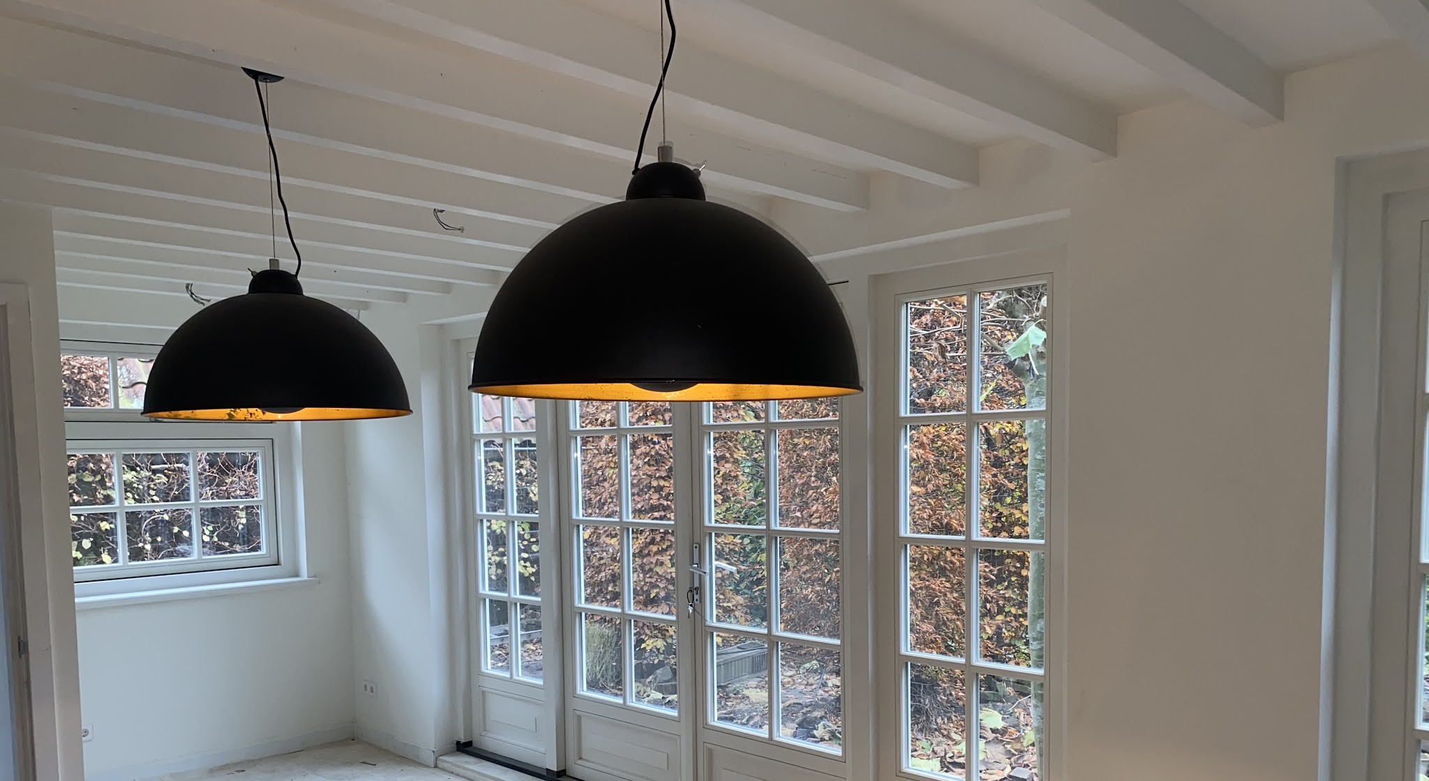 Twee zwarte hanglampen, aangesloten boven een serre met openslaande deuren